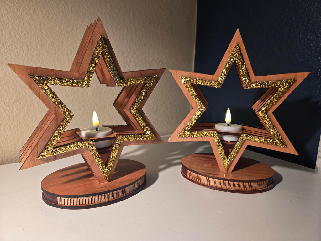 Two laser-cut wood star candle holders with gold glitter accents and lit tealights