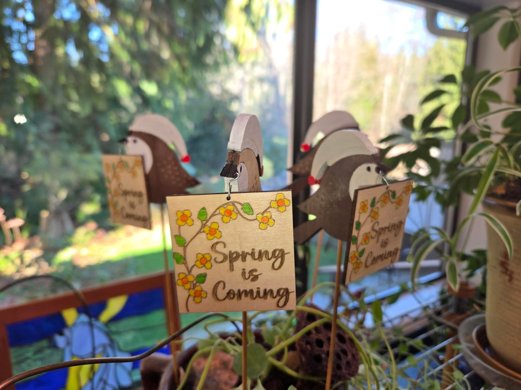 Close-up of Spring is Coming engraved wood sign with yellow painted flowers hanging from chickadee stake