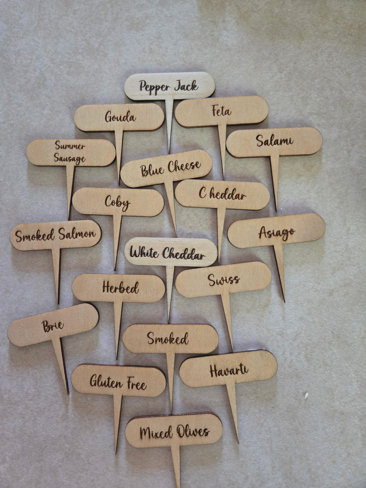 All 18 laser engraved charcuterie labels spread out showing label names including Pepper Jack, Gouda, Feta, Salami, Blue Cheese, Cheddar, Brie, Swiss, Mixed Olives and more